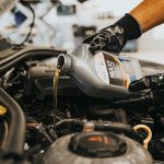 A close-up of a mechanic in gloves pouring engine oil into a car engine, showcasing automotive maintenance.