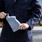 Close-up of a mechanic in a blue uniform holding a gray oil container on a city street.